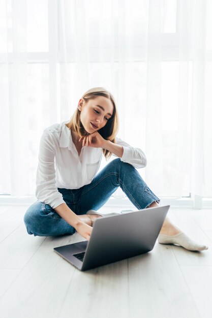 Attractive young woman surfing on her laptop sitting on the floor