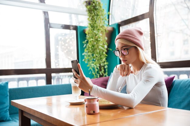 Привлекательная молодая женщина, принимая селфи с мобильного телефона в кафе