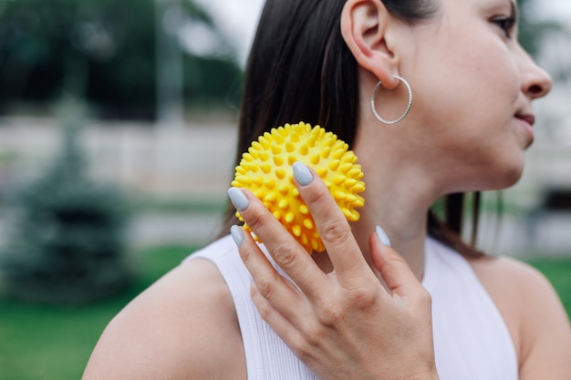 Attractive young woman use spiky massage ball to tighten skin and improve blood circulation in muscles in park in summer.