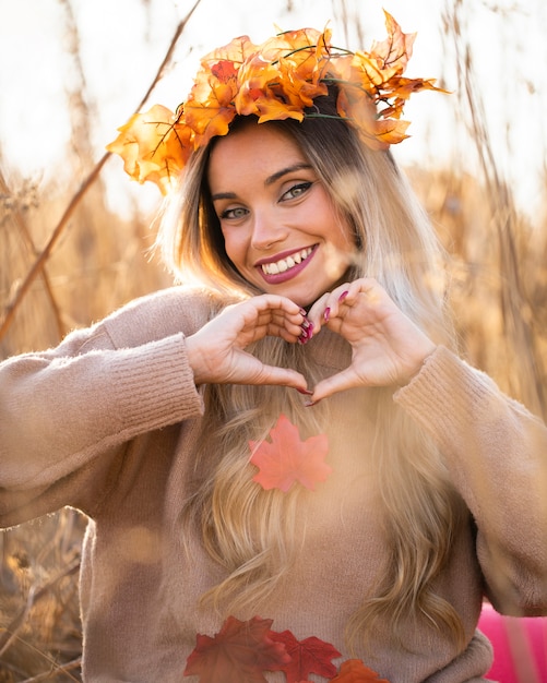 Attractive young woman wearing maple leaves tiara making heart shape with hand