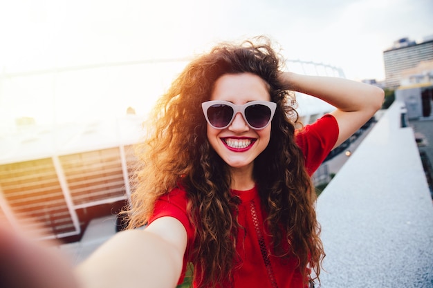 Attractive young woman with curly hair takes a selfie, posing and looking at camera