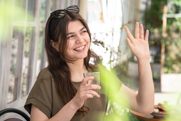 カフェのテラスで夏の日にコップ一杯の水を持つ魅力的な若い女性