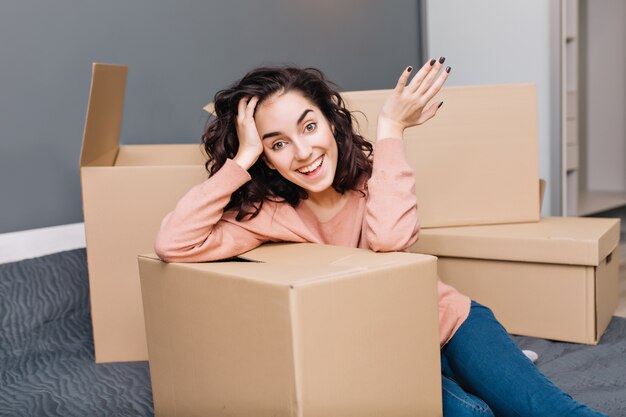 Attractive young woman with short brunette curly hair expressing suround carton in modern appartment. Enjoying relocation, moving to new home, true happy emotions