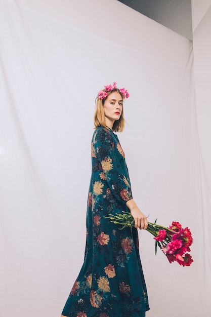 Attractive young woman with wreath on head and bunch of flowers