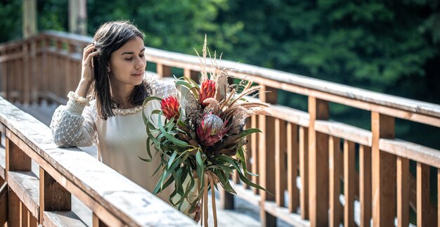 木製の橋の上の魅力的な若い女性は、エキゾチックな花の花束を持って立っています。