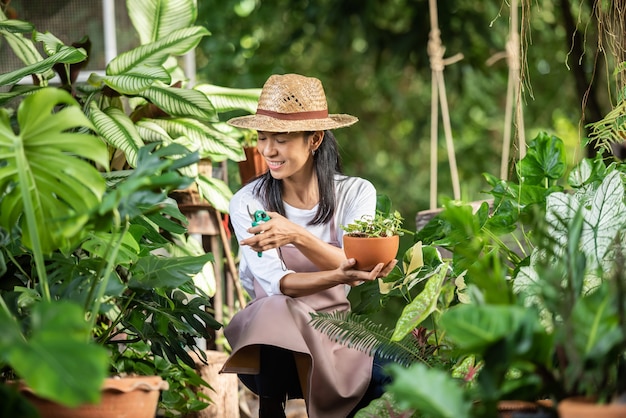 Free photo attractive young woman working with decorative plants in garden center. female supervisor examining plants in gardening outside in summer nature. beautiful gardener smiling. plant care.