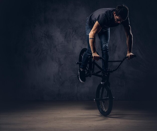 Сaucasian man, makes an acrobatic figure with BMX in a studio. Isolated on a dark background.