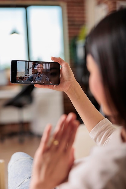 Настоящая занятая азиатская женщина по видеозвонку встречается с онлайн-коммуникациями из дома. говорящее мобильное приложение машет привет интернет технологии счастливый звонок бизнес фрилансер говорить