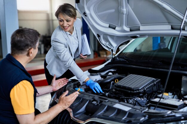 Auto mechanic and businesswoman cooperating while checking under vehicle hood in a workshop