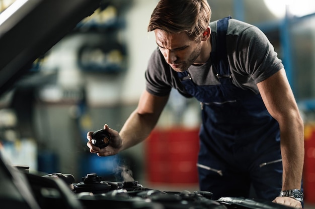 Auto mechanic opening radiator cap and checking overheated car cooling system in a workshop