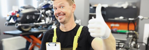 Auto mechanic showing thumb up and holding documents in repair shop quality motorcycle repair