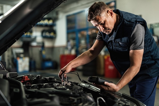 Auto mechanic using diagnostic tool while checking car battery voltage in a workshop