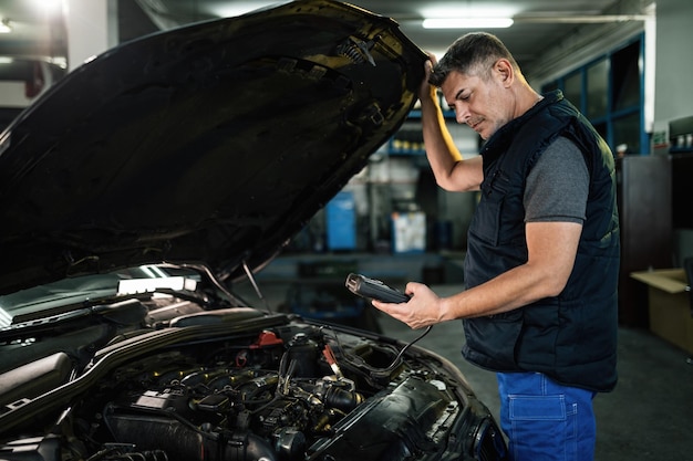 Free photo auto mechanic using diagnostic work tool while checking car engine in a workshop