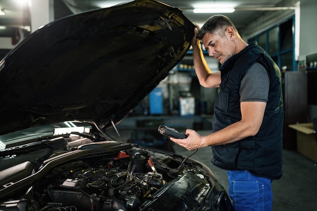 ワークショップで車のエンジンをチェックしながら診断作業ツールを使用して自動車整備士