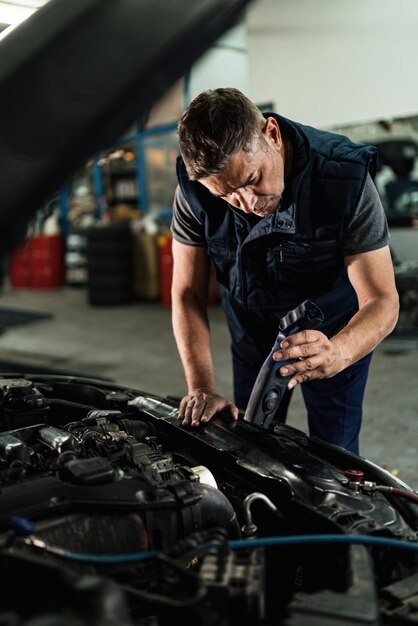 Auto mechanic using lamp while analyzing car engine in a workshop