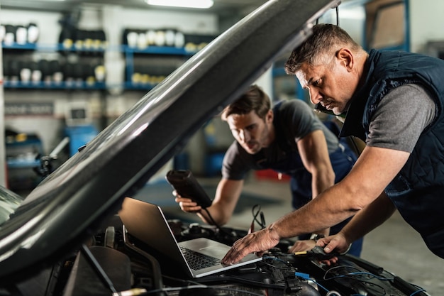 Free photo auto mechanic using laptop and cooperating with a coworker while doing car diagnostic in repair shop