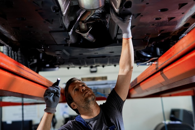 Auto repairman examining undercarriage of a car in a workshop