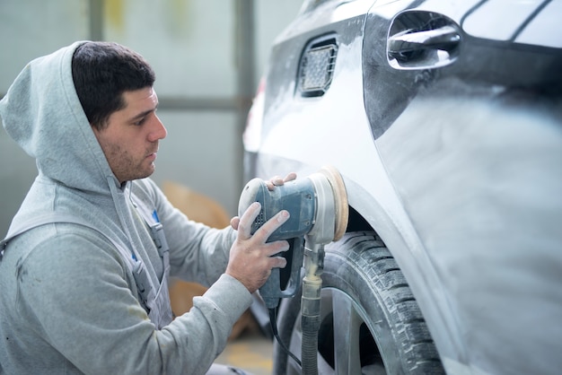 塗装用車両準備機で車体を研削する自動車修理工