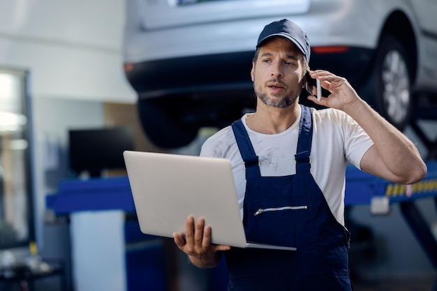 Riparatore automatico che parla al telefono mentre utilizza il laptop in un'officina