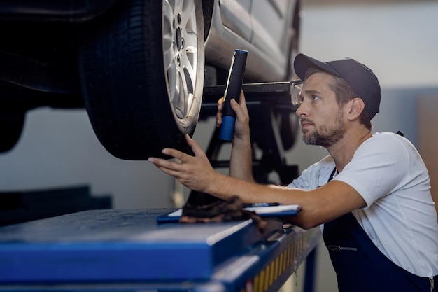 Auto repairman using flashlight while examining car tire in a workshop