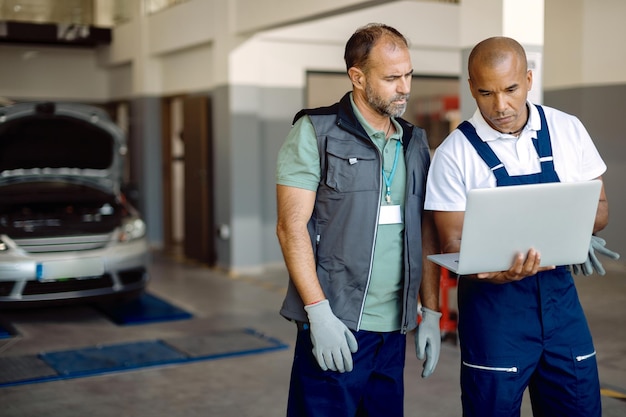 auto repairmen cooperating while working on laptop at car service workshop