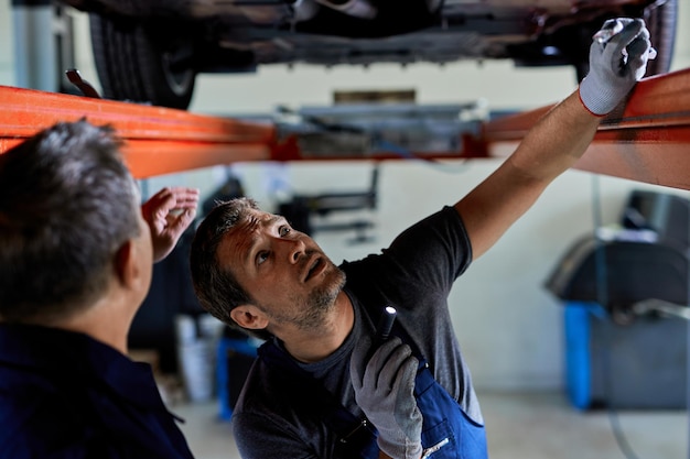 Auto repairmen examining undercarriage of a car in a workshop