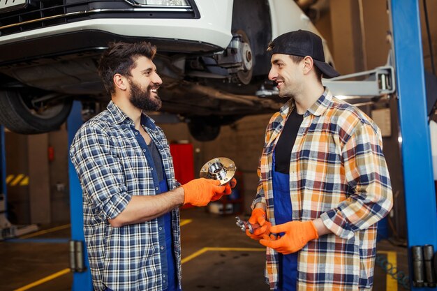 Automechanics with lifted car on the background in the service station talking about car detail