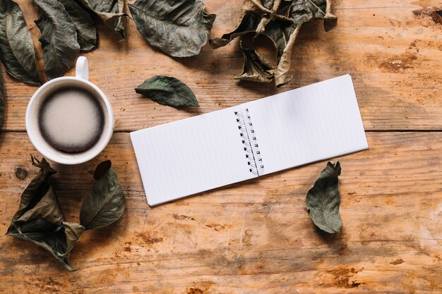 Autumn composition with dried leaves, cup of coffee and notebook