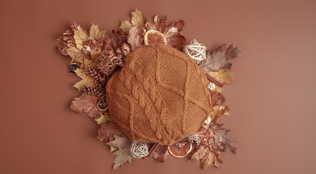 Autumn composition with leaves, pine cones and round knitted element on brown background copy space.