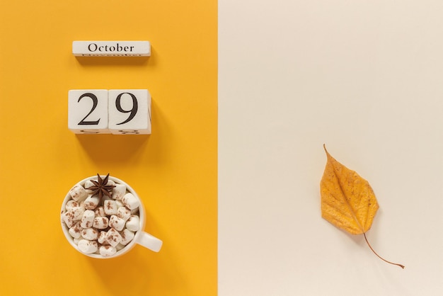 Autumn composition. wooden calendar october 29, cup of cocoa with marshmallows and yellow autumn leaves on yellow beige background. top view flat lay mockup concept hello september.