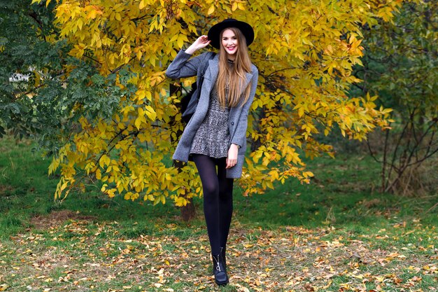 Autumn fashion portrait of elegant glamour woman posing at amazing city park, stylish coat ,backpack and vintage hat. Walking alone , cold weather