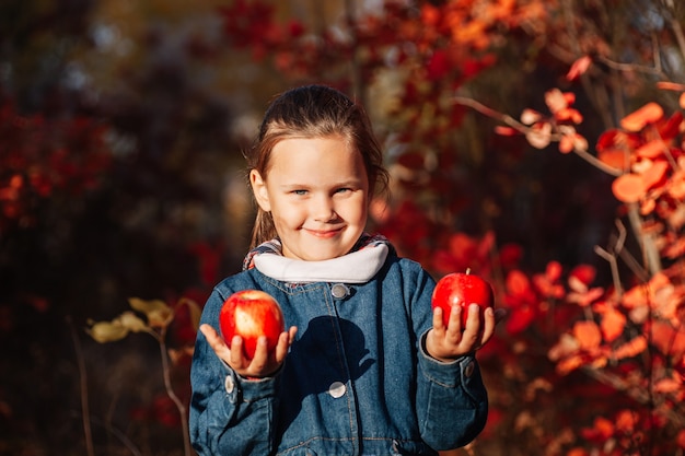 Autumn forest concept cute happy girl in jeans coat hold big red apple with autumn background