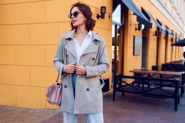 Autumn image of stylish charming female in beige coat walking outdoor. Fashionable street look.