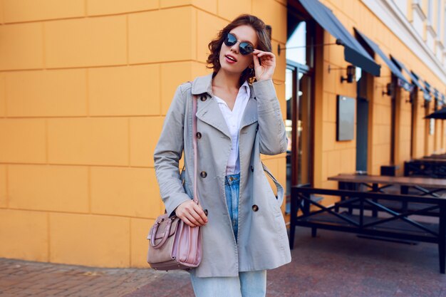 Autumn image of stylish charming female in beige coat walking outdoor. Fashionable street look.