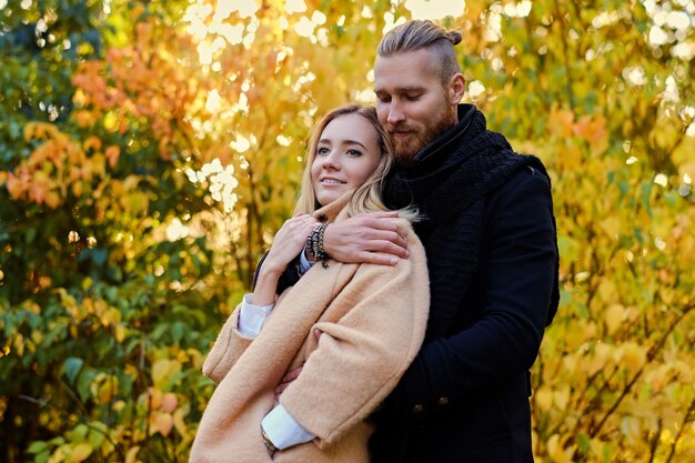 Autumn love story. Attractive redhead male hugs cute blonde female in autumn wild nature background.