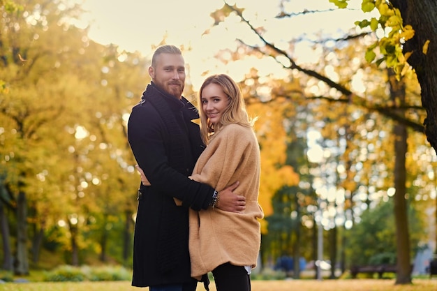 Autumn love story. Attractive redhead male hugs cute blonde female in autumn wild nature background.