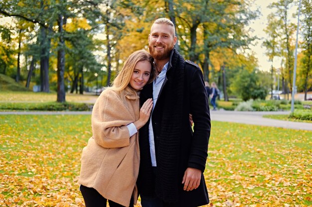 Autumn love story. Attractive redhead male hugs cute blonde female in autumn wild nature background.