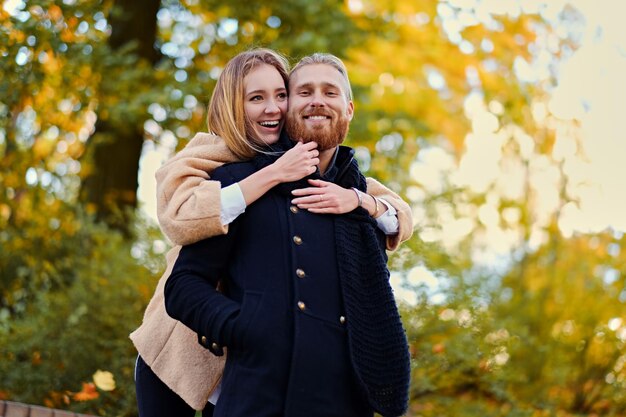 秋の童話。赤毛のひげを生やした男性は、秋の公園でデートでかわいい金髪の女性を抱きしめます。