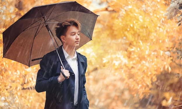 Autumn park in rainy weather and a young man with an umbrella