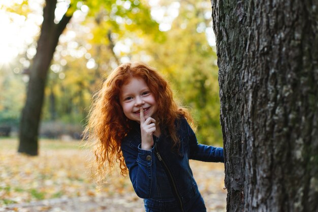 Осенние флюиды, детский портрет. Очаровательная и рыжая девочка выглядит счастливой, прогуливаясь и играя