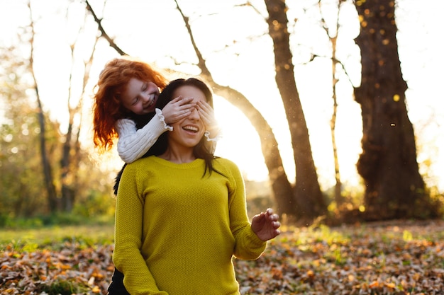 秋の雰囲気、家族の肖像画。魅力的なママと彼女の赤い髪の娘は、落ちた人の上に座って楽しんでいます