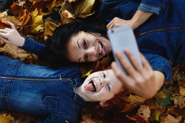 Autumn vibes, family portrait. Charming mom and her red hair daughter have fun taking a selfie on sm