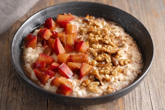 Autumnal porridge with plums, walnuts and honey served in bowl on wooden table.