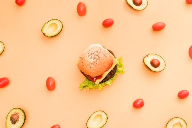 Бесплатное фото Авокадо и помидоры черри в окружении гамбургера на цветном фоне