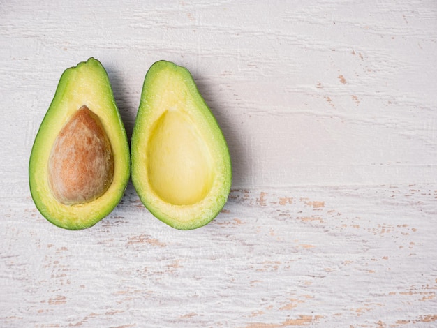 Avocado cut in half on white wooden board.