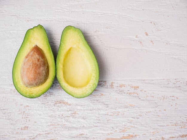 Avocado cut in half on white wooden board.