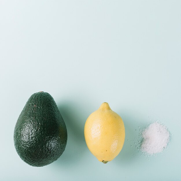 Авокадо лимон и соль расположены в ряд на зеленом фоне