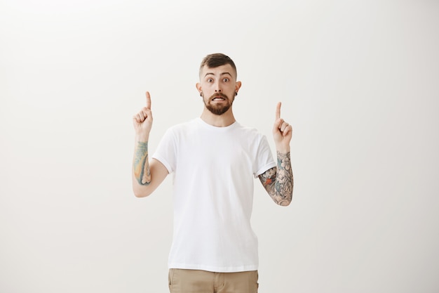 Awkward and astounded hipster guy looking startled and pointing fingers up