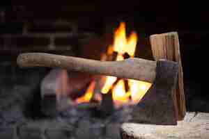 Foto gratuita un'ascia conficcata in un ceppo di legno vicino a un caminetto acceso. il concetto di comfort e relax nel villaggio.