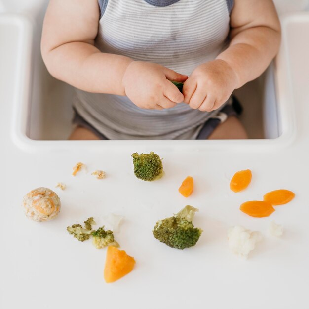 Free photo baby boy in highchair eating vegetables alone